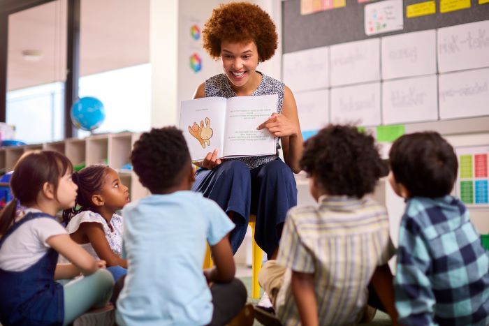 Foto de professora em sala de aula de Educação Infantil contando uma história aos alunos com livro ilustrado.